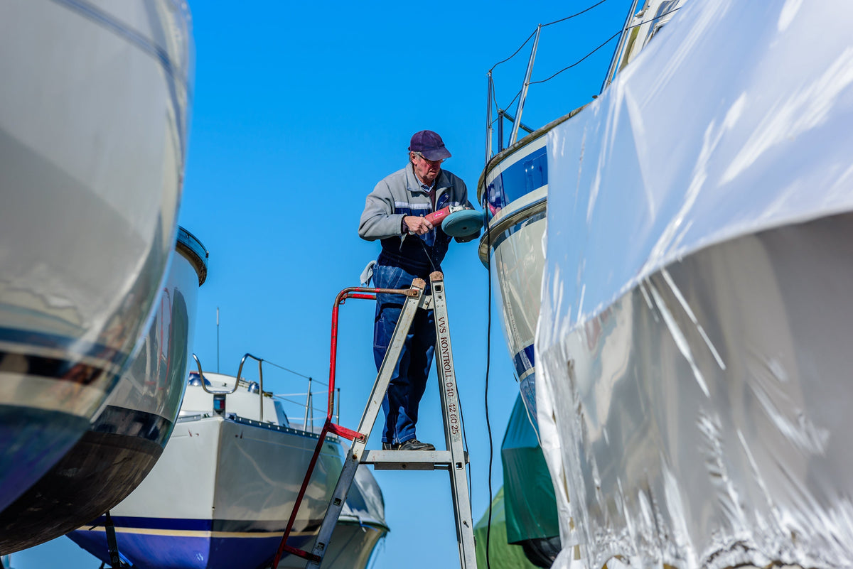 a man on a ladder  removing oxidation from the side of a boat