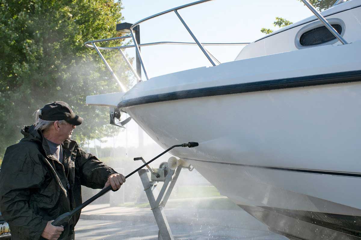 a man pressure washing the hull of a white boat
