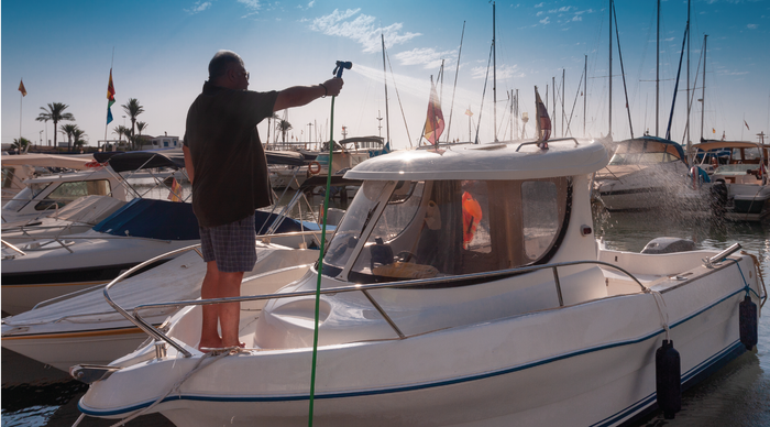 A man standing on the bow of a boat hosing it down