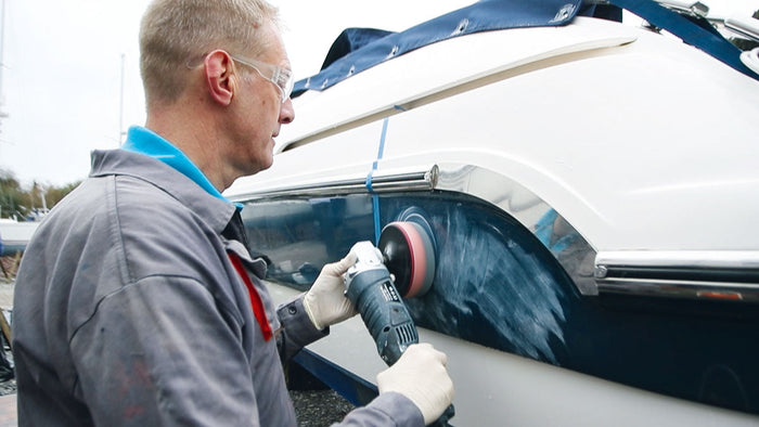a man with safety glasses buffing the side of a boat