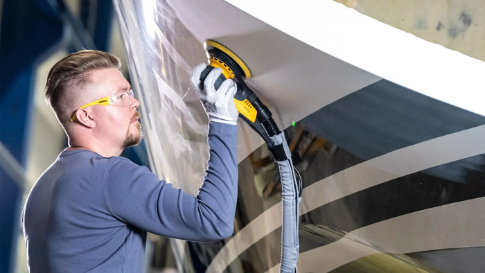 a man wearing safety glasses buffing a boat