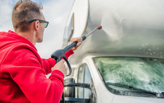 a man with sunglasses on pressure washing the front of an RV