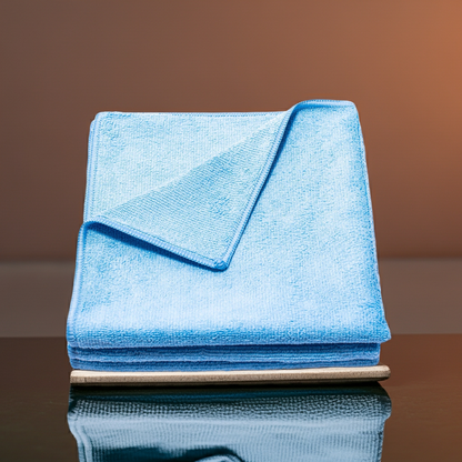 Stack of blue Poli Glow 320 GSM microfiber cloths on a reflective surface with a brown background
